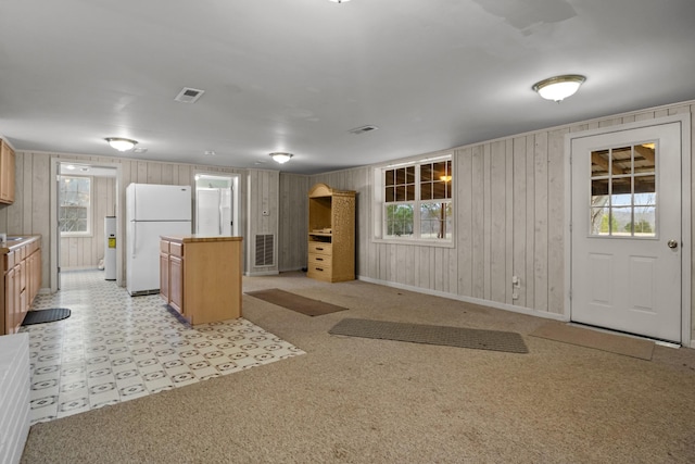 kitchen with wooden walls, light colored carpet, a kitchen island, and white fridge