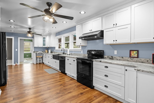 kitchen with sink, black appliances, light wood-type flooring, light stone countertops, and white cabinets