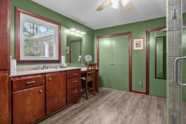 bathroom with hardwood / wood-style floors, a shower with shower door, vanity, ceiling fan, and a textured ceiling