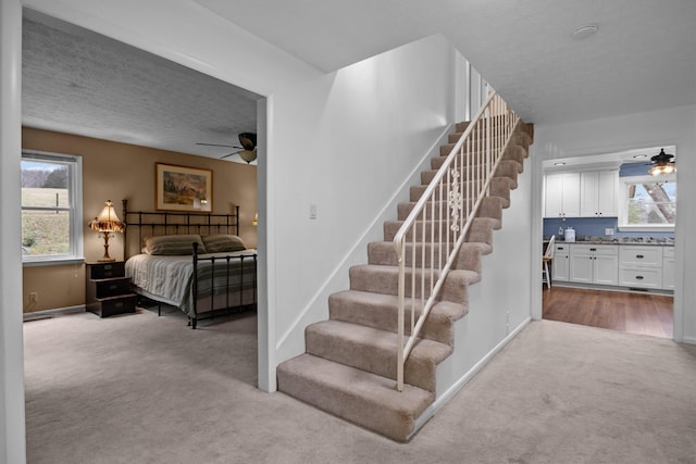 stairway with ceiling fan, carpet flooring, and a textured ceiling