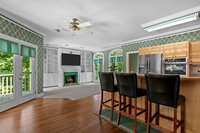 kitchen featuring stainless steel fridge, a breakfast bar, wall oven, a high end fireplace, and ornamental molding