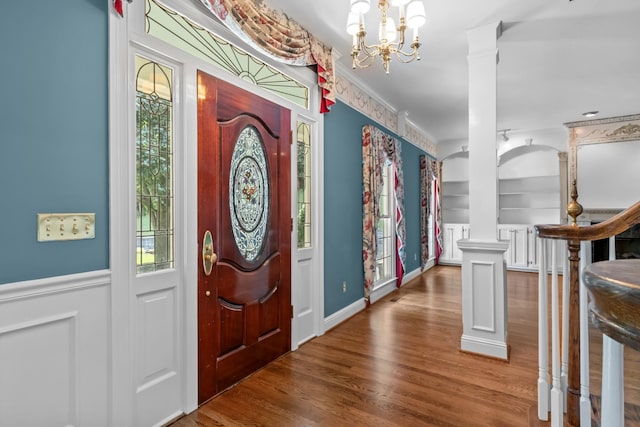 foyer featuring ornate columns, ornamental molding, an inviting chandelier, and dark hardwood / wood-style flooring