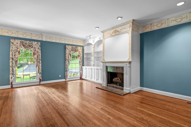 unfurnished living room with built in shelves, ornamental molding, wood-type flooring, and a premium fireplace