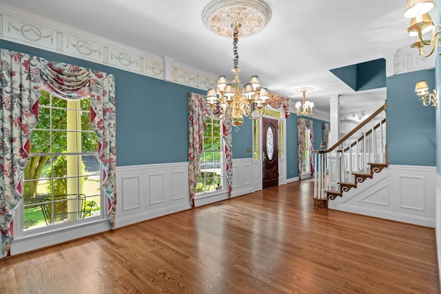 entryway with wood-type flooring, ornamental molding, and a notable chandelier