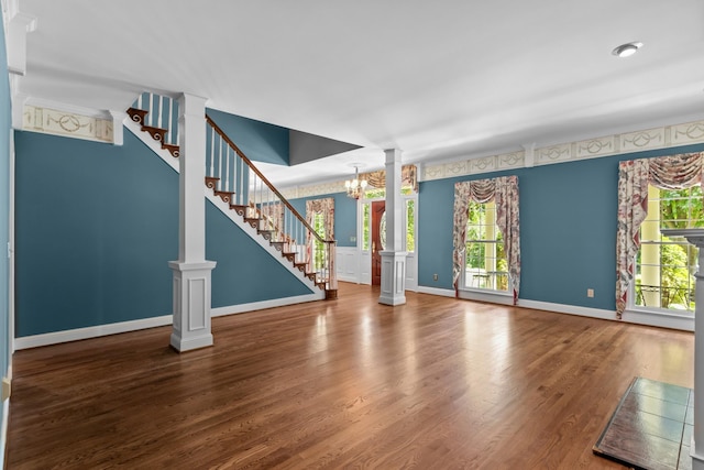 unfurnished living room with a notable chandelier, a wealth of natural light, hardwood / wood-style floors, and ornate columns