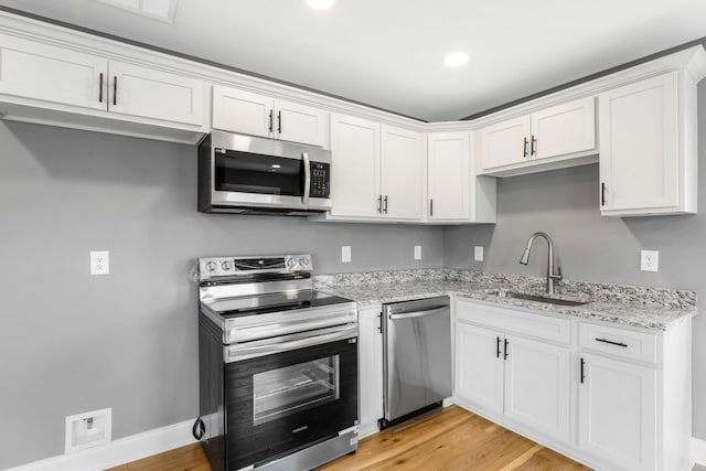 kitchen with sink, light hardwood / wood-style flooring, white cabinetry, stainless steel appliances, and light stone countertops