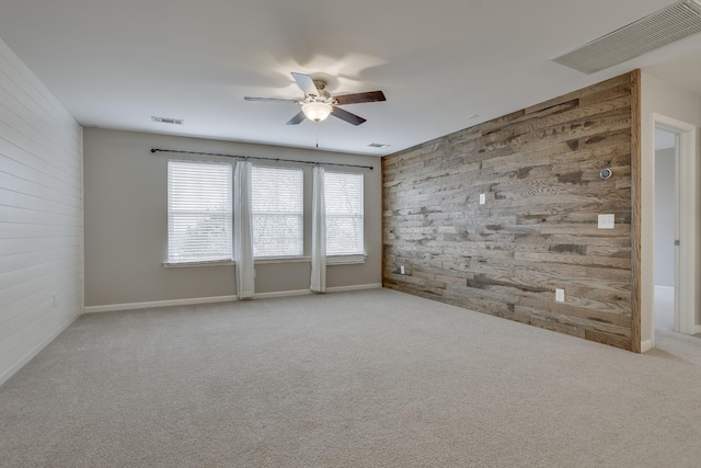 carpeted spare room featuring wooden walls and ceiling fan