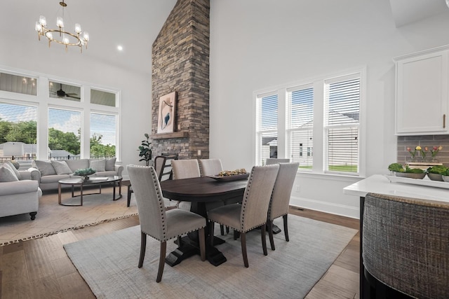 dining space with a stone fireplace, a chandelier, light hardwood / wood-style flooring, and a high ceiling