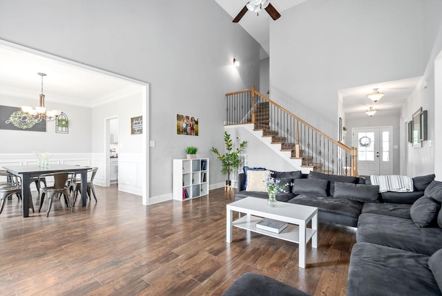 living room with a towering ceiling, ornamental molding, dark hardwood / wood-style floors, and ceiling fan with notable chandelier