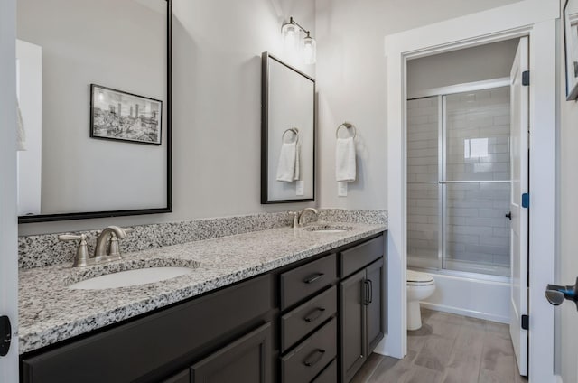 full bathroom featuring vanity, toilet, combined bath / shower with glass door, and wood-type flooring