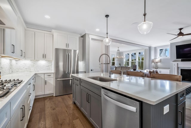 kitchen with appliances with stainless steel finishes, sink, white cabinets, hanging light fixtures, and a kitchen island with sink