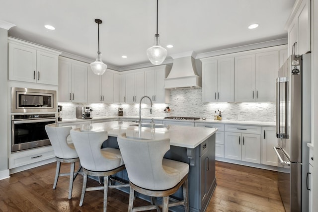 kitchen with a center island with sink, custom exhaust hood, white cabinets, and appliances with stainless steel finishes