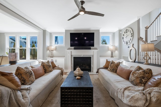 living room with a premium fireplace, ornamental molding, and ceiling fan