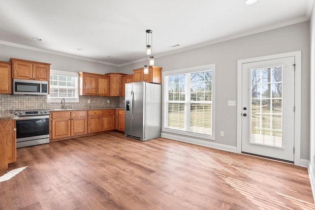 kitchen with pendant lighting, crown molding, appliances with stainless steel finishes, tasteful backsplash, and light wood-type flooring