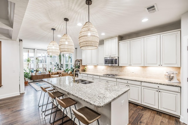 kitchen with white cabinetry, stainless steel appliances, decorative light fixtures, and an island with sink