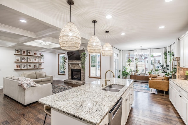 kitchen featuring an island with sink, white cabinetry, sink, hanging light fixtures, and light stone counters