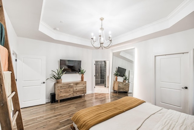 bedroom with crown molding, connected bathroom, a tray ceiling, wood-type flooring, and a chandelier