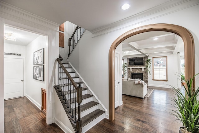 stairs featuring a stone fireplace, hardwood / wood-style floors, beamed ceiling, coffered ceiling, and crown molding