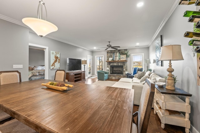 dining space featuring crown molding, a stone fireplace, hardwood / wood-style floors, and ceiling fan