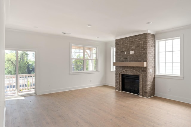 unfurnished living room featuring ornamental molding, plenty of natural light, a brick fireplace, and light wood-type flooring