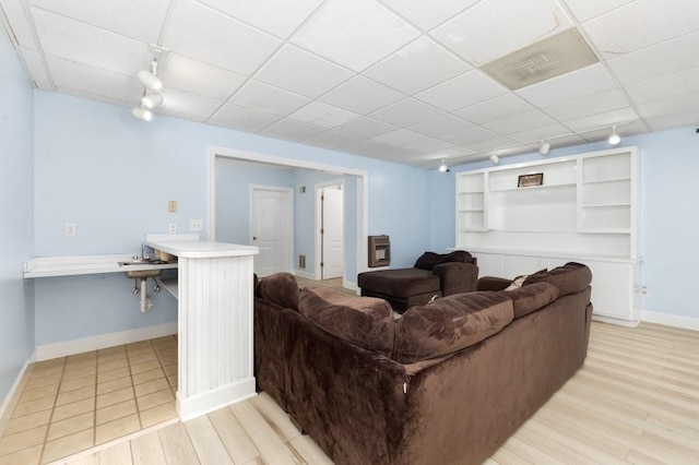 living room with built in shelves, a paneled ceiling, rail lighting, and light wood-type flooring