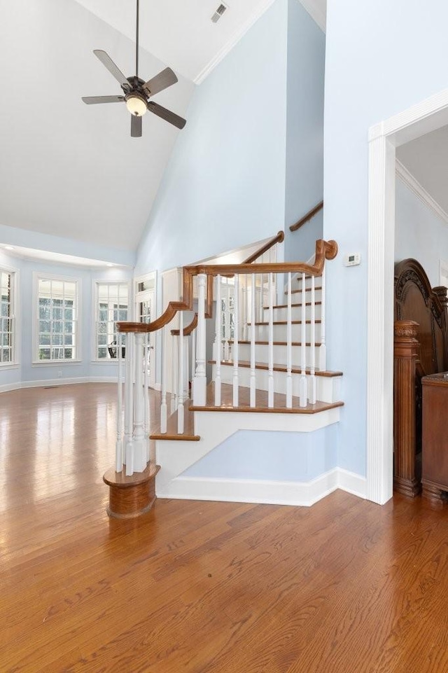 stairway with wood-type flooring, ornamental molding, ceiling fan, and high vaulted ceiling