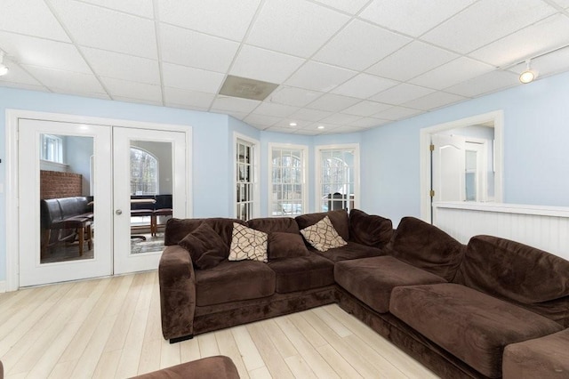 living room with a drop ceiling, french doors, and light wood-type flooring