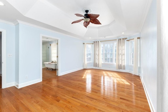 empty room with ceiling fan, ornamental molding, a raised ceiling, and light hardwood / wood-style floors