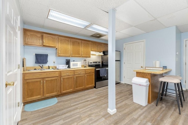 kitchen featuring sink, a breakfast bar, appliances with stainless steel finishes, light hardwood / wood-style floors, and a drop ceiling