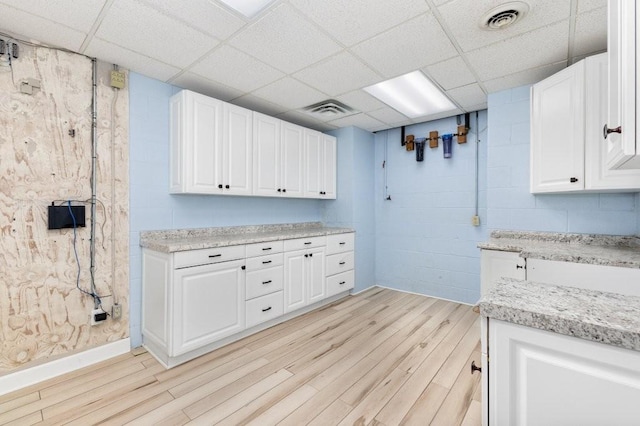 kitchen with a drop ceiling, light hardwood / wood-style floors, and white cabinets