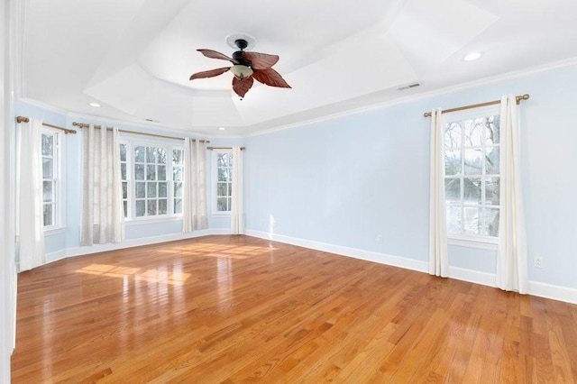 empty room featuring a raised ceiling, ornamental molding, and light wood-type flooring