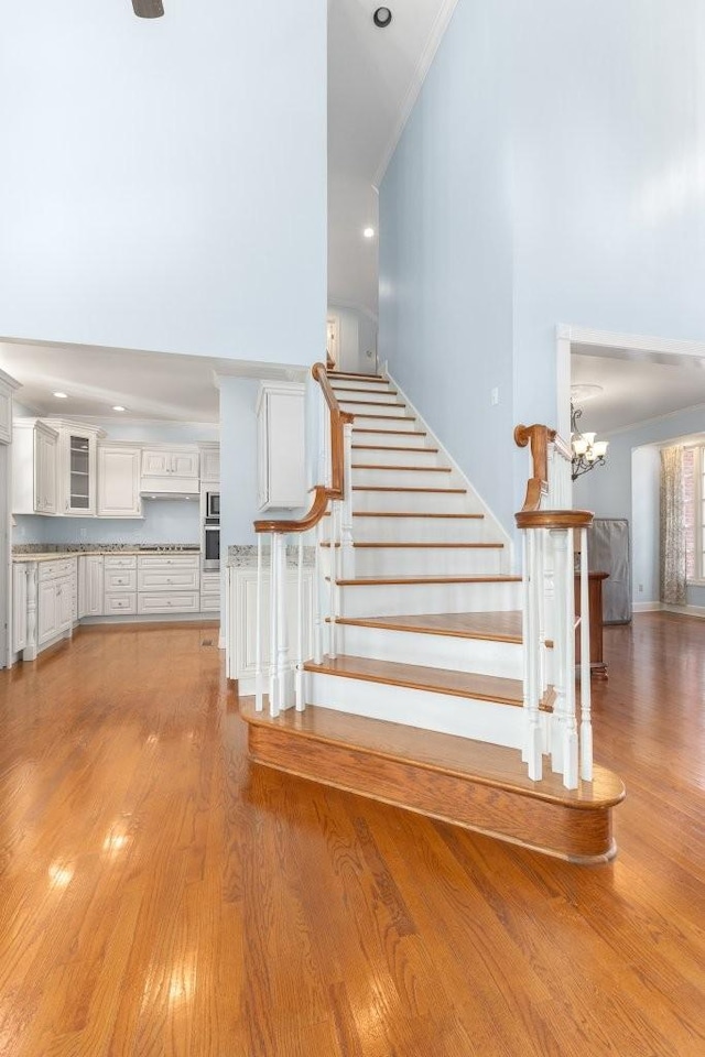 staircase featuring an inviting chandelier, ornamental molding, hardwood / wood-style floors, and a high ceiling