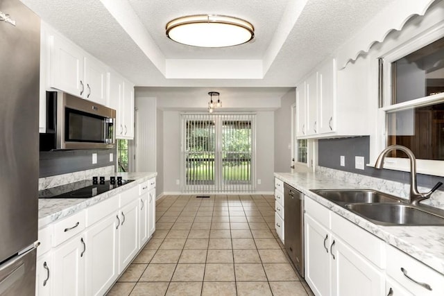 kitchen featuring appliances with stainless steel finishes, white cabinetry, sink, light tile patterned floors, and a tray ceiling