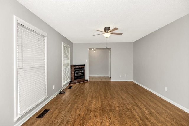 unfurnished living room with a brick fireplace, dark wood-type flooring, a textured ceiling, and ceiling fan