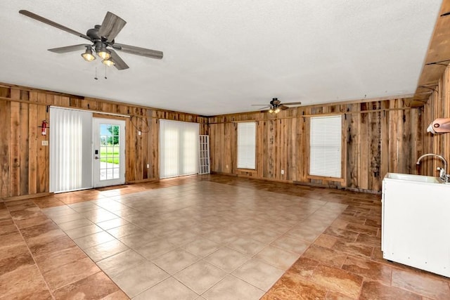 empty room with a textured ceiling, wooden walls, and ceiling fan