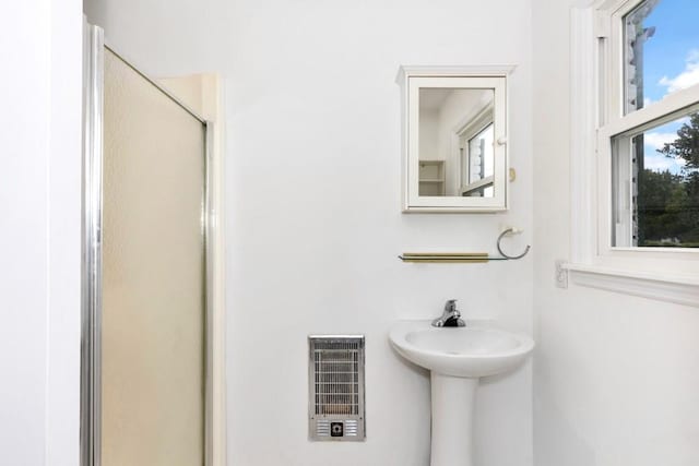 bathroom with sink, heating unit, and a shower with shower door