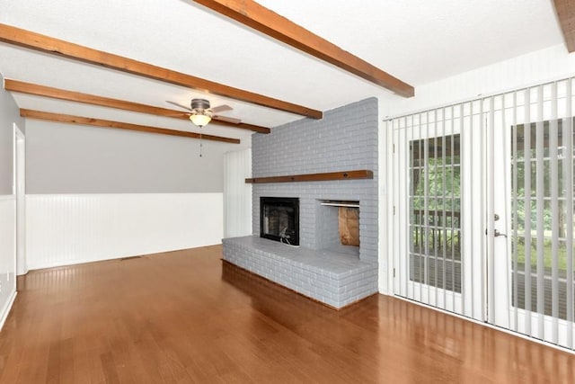 unfurnished living room with ceiling fan, hardwood / wood-style floors, a textured ceiling, a brick fireplace, and beamed ceiling