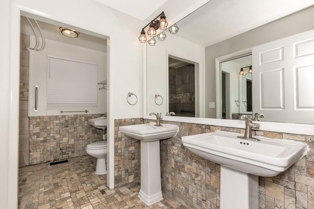 bathroom featuring dual sinks, tile walls, and toilet