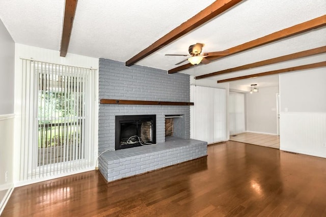 unfurnished living room featuring a fireplace, wood-type flooring, ceiling fan, a textured ceiling, and beam ceiling