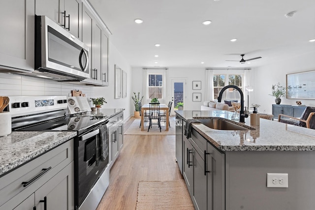 kitchen with sink, gray cabinetry, a center island with sink, stainless steel appliances, and backsplash