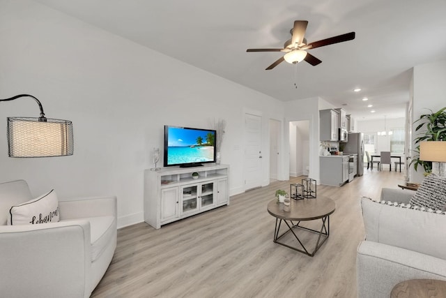 living area featuring light wood-style flooring, recessed lighting, ceiling fan with notable chandelier, and baseboards