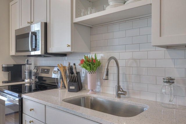 kitchen with appliances with stainless steel finishes, sink, white cabinets, and light stone counters