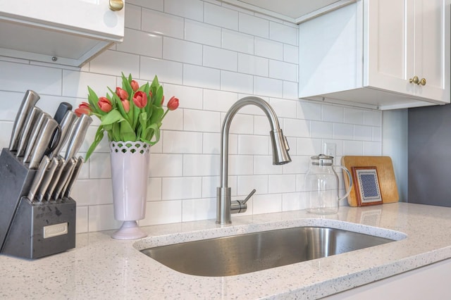 interior details with sink, backsplash, white cabinets, and light stone counters