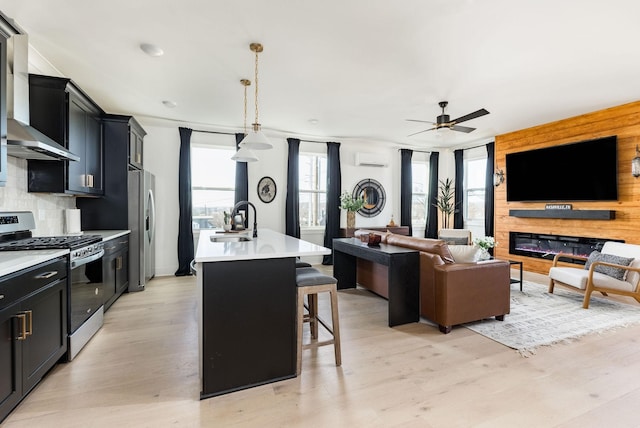 kitchen featuring pendant lighting, wall chimney range hood, a breakfast bar area, appliances with stainless steel finishes, and an island with sink