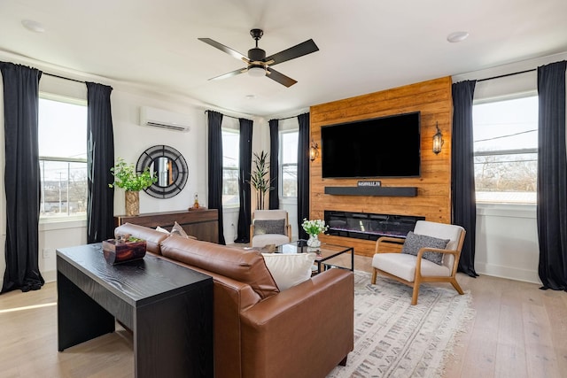 living room featuring a large fireplace, a wall mounted AC, ceiling fan, and light hardwood / wood-style flooring