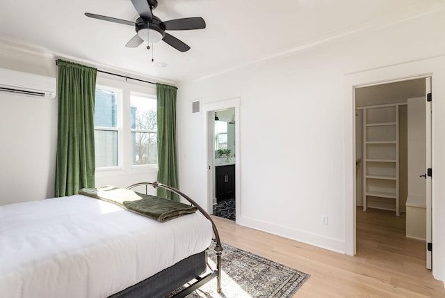 bedroom featuring ceiling fan, an AC wall unit, ensuite bathroom, and light wood-type flooring