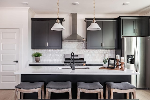 kitchen with decorative light fixtures, sink, a kitchen island with sink, stainless steel appliances, and wall chimney range hood