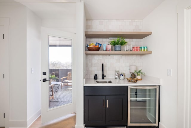 bar with sink, backsplash, light hardwood / wood-style floors, and beverage cooler