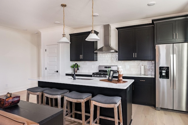 kitchen featuring wall chimney exhaust hood, stainless steel appliances, a center island with sink, and pendant lighting