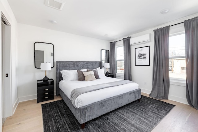 bedroom featuring multiple windows, light hardwood / wood-style floors, and a wall unit AC